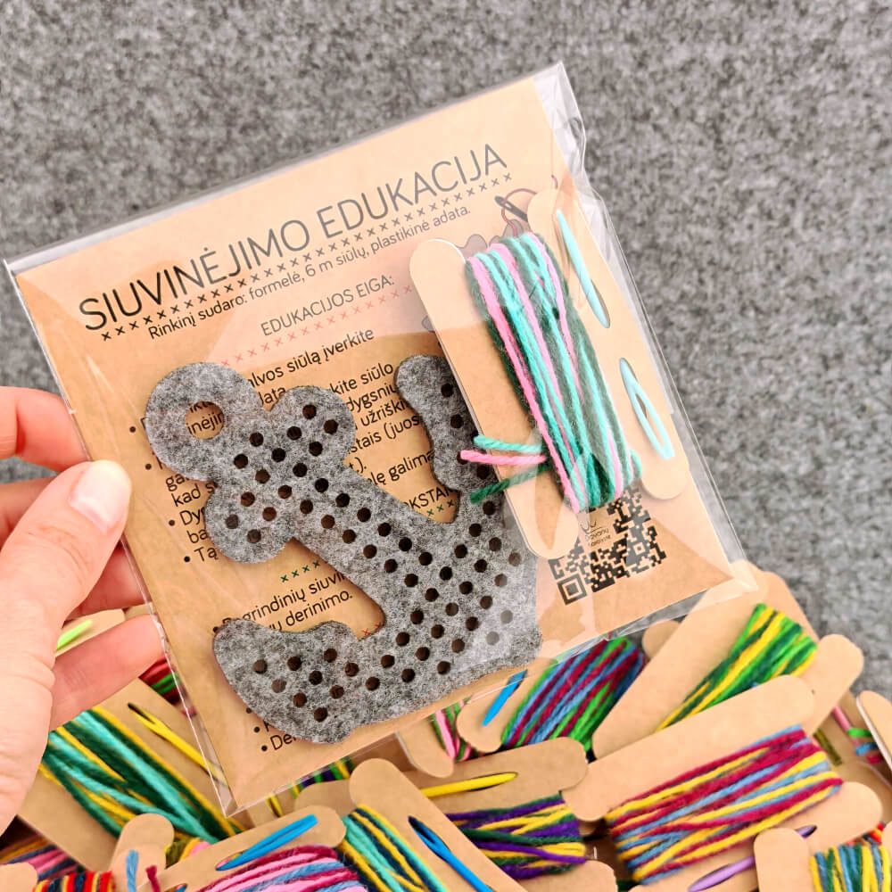Skaidrioje plastikinėje pakuotėje supakuotas siuvinėjimo edukacinis rinkinys „Inkaras“ su instrukcija ir dalomąja medžiaga.