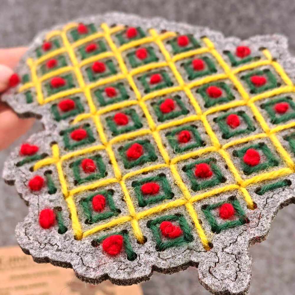 ankoje laikomas pilnai išsiuvinėtas veltinio Lietuvos žemėlapis su geometriniu langelių raštu iš geltonų, žalių ir raudonų siūlų.